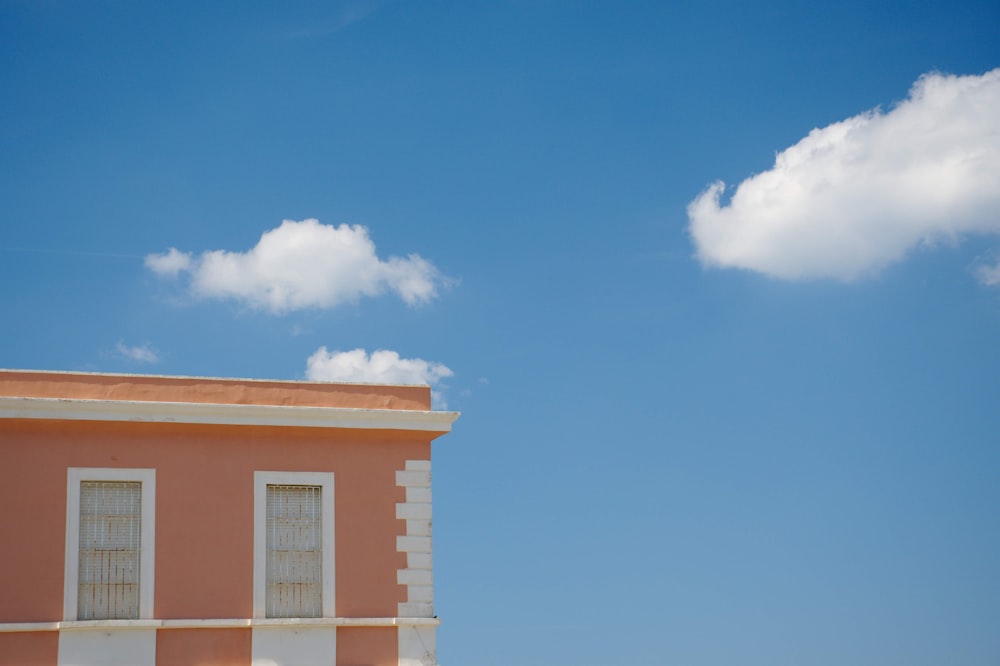 um edifício rosa com duas janelas e uma nuvem branca no céu