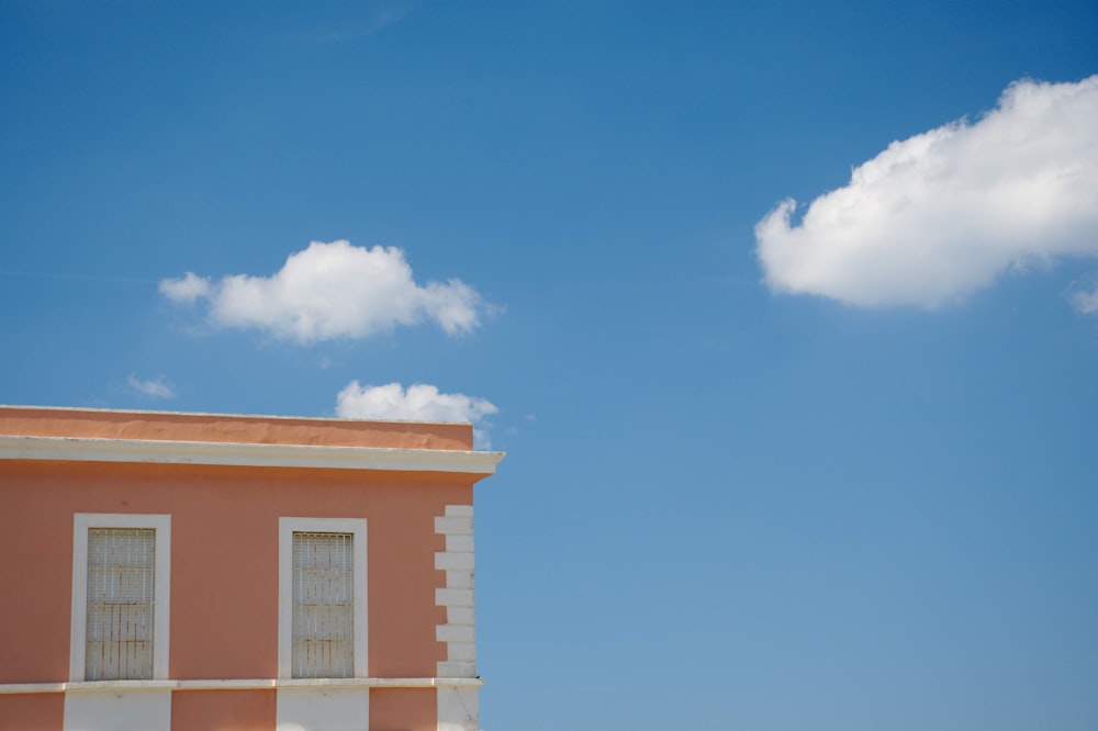 a pink building with two windows and a white cloud in the sky