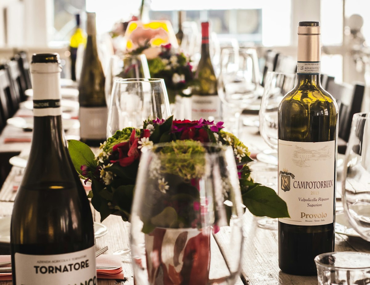 Several bottles of red wine lined up on a table with labels facing forward in warm light