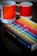 A book titled 'The Secret Lives of Colour' with a vibrant cover featuring various colorful stripes is placed on a dark surface. Next to it are two ceramic mugs with a color gradient design, labeled with Pantone color codes.