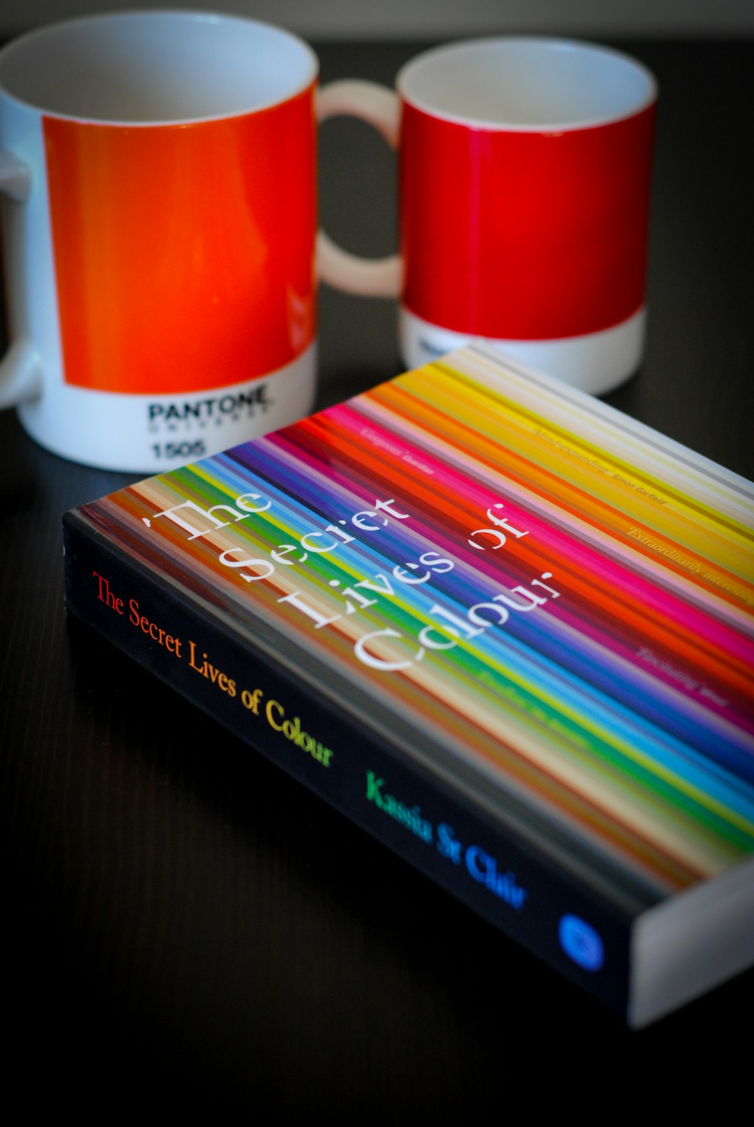 two white-and-red ceramic mugs near The Secret Lives of Colour book