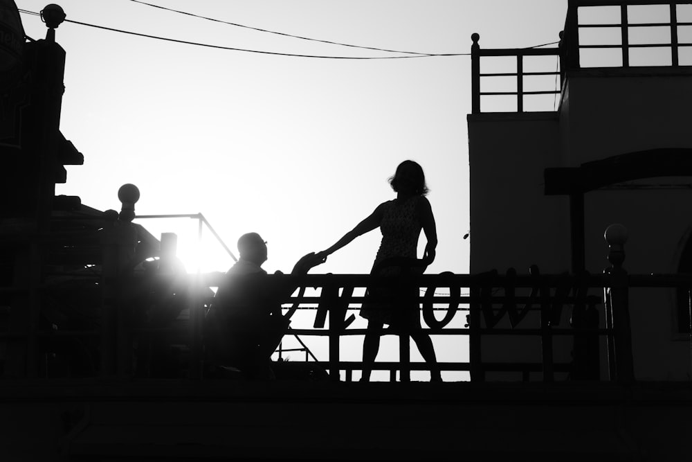 silhouette of girl standing near man kneeling beside railing
