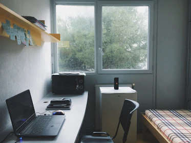 A bright, tidy student room with a comfortable bed and study desk by the window.