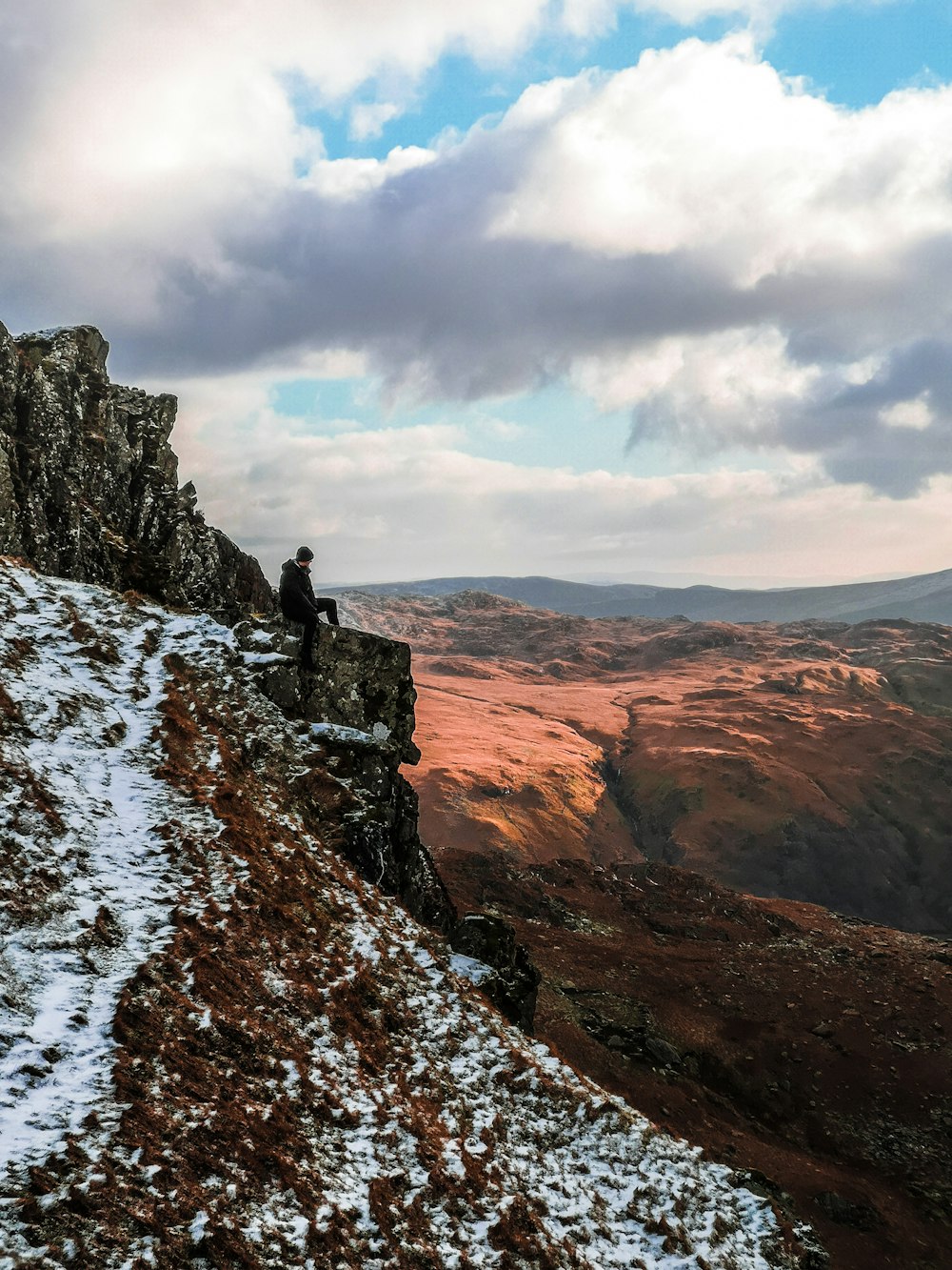 man wearing black jacket sitting on cliff