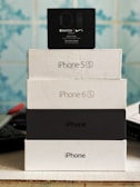 Stack of electronic device boxes, including an Apple Watch Series 3 box on top, followed by two iPhone boxes, with model names iPhone 5S and iPhone 6S.