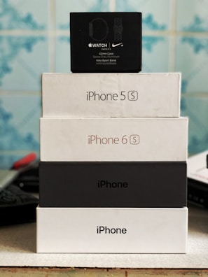 Stack of electronic device boxes, including an Apple Watch Series 3 box on top, followed by two iPhone boxes, with model names iPhone 5S and iPhone 6S.
