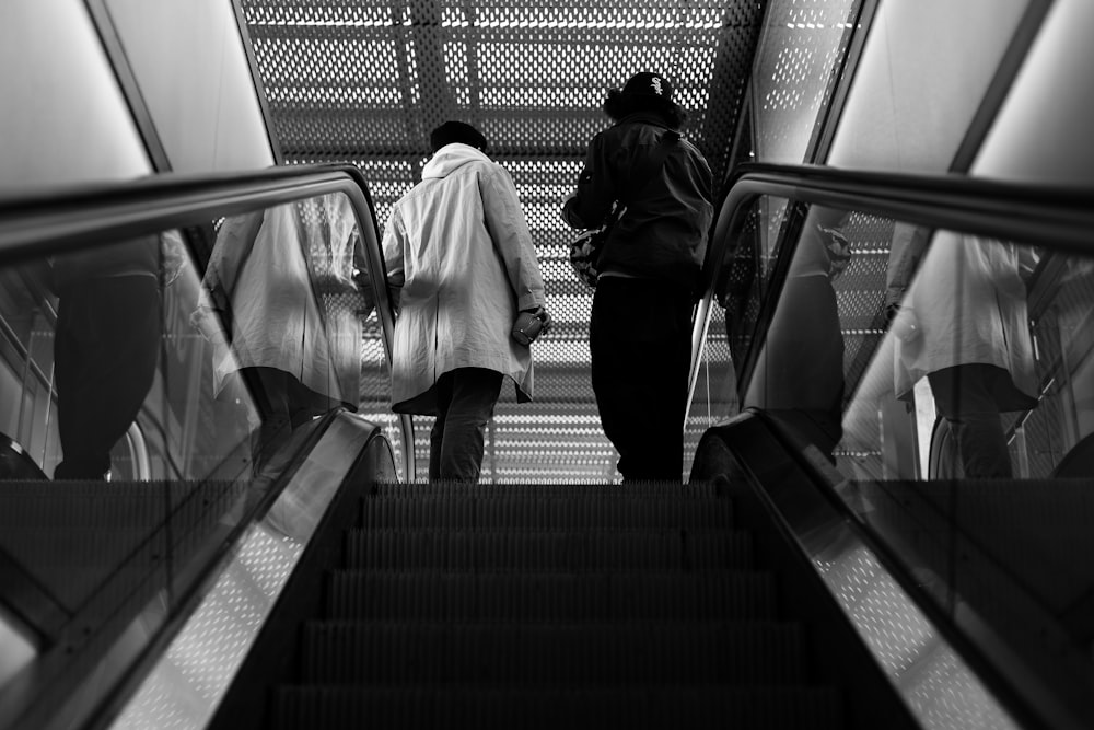 grayscale photography of two person riding scalator