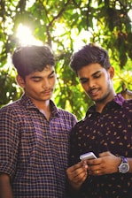 two men standing under green tree