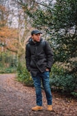 An outdoor shot of a model in a soft olive green jacket and matching boots, standing among autumn leaves.