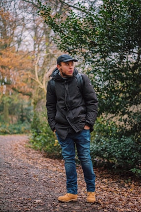 An outdoor shot of a model in a soft olive green jacket and matching boots, standing among autumn leaves.