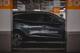 A sleek, modern car is parked in an indoor parking space. The vehicle is metallic gray with a glossy finish and features alloy wheels. It is positioned between two concrete pillars, marked with the number 50 in large orange font. The branding 'Nouveau Renault Kadjar' and 'Test Drive' is visible on the side of the car. The surrounding area is dimly lit, contributing to a sophisticated atmosphere.