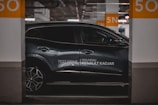 A sleek, modern car is parked in an indoor parking space. The vehicle is metallic gray with a glossy finish and features alloy wheels. It is positioned between two concrete pillars, marked with the number 50 in large orange font. The branding 'Nouveau Renault Kadjar' and 'Test Drive' is visible on the side of the car. The surrounding area is dimly lit, contributing to a sophisticated atmosphere.