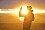 A silhouette of a man standing on a hill at sunrise, arms raised in worship.