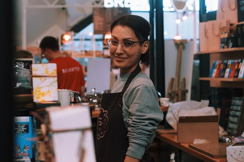 A local café owner serving customers with a warm smile behind the counter.