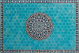 A detailed Islamic geometric pattern featuring a central circular design with intricate interlocking shapes crafted from blue, white, and green colors. This is set against a background of hexagonal turquoise tiles, bordered by a smaller repeating triangular pattern.