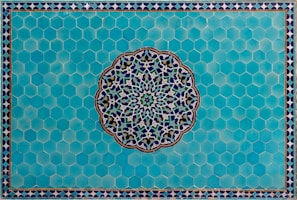 A detailed Islamic geometric pattern featuring a central circular design with intricate interlocking shapes crafted from blue, white, and green colors. This is set against a background of hexagonal turquoise tiles, bordered by a smaller repeating triangular pattern.