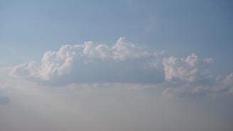A large, fluffy white cloud floating in a clear blue sky with a soft gradient towards the horizon.