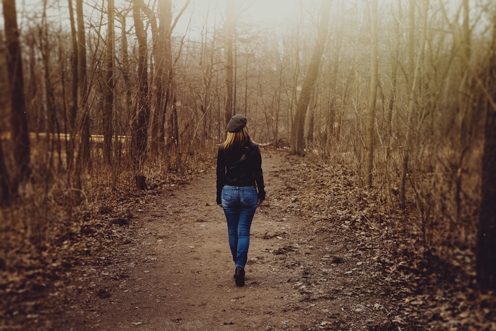 Femme en pull noir et jean skinny en denim bleu marche sur un chemin de terre à côté d’arbres sans feuilles