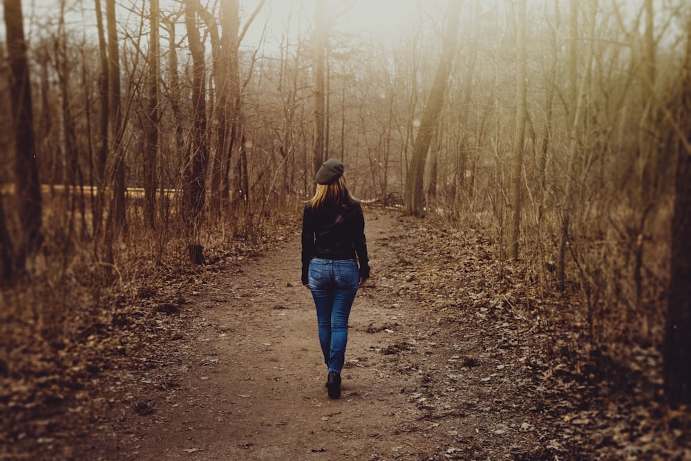 Mujer con suéter negro y jeans ajustados de mezclilla azul camina por camino de tierra junto a árboles sin hojas