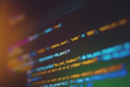 A close-up view of a computer screen displaying lines of code. The background is dark, and the text appears in various colors such as blue, orange, and green, providing contrast and focus on the programming syntax.