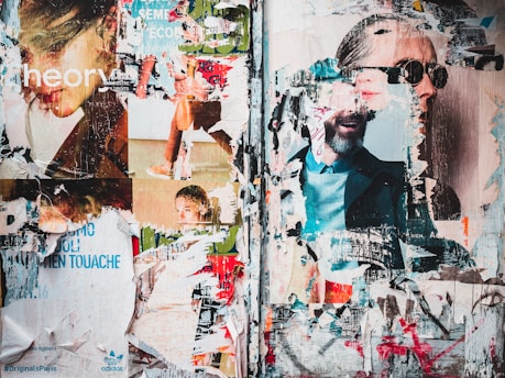 A collage of torn and layered posters on a wall, featuring fragmented images of people, texts, and logos. The layers reveal parts of faces, some wearing sunglasses, and various printed advertisements. The overlapping textures create a chaotic yet intriguing composition.