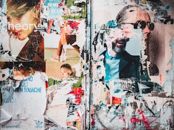 A collage of torn and layered posters on a wall, featuring fragmented images of people, texts, and logos. The layers reveal parts of faces, some wearing sunglasses, and various printed advertisements. The overlapping textures create a chaotic yet intriguing composition.