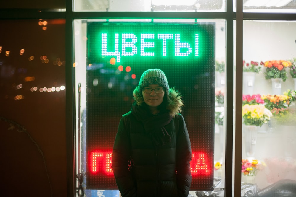 woman wearing black parka coat standing near neon signage