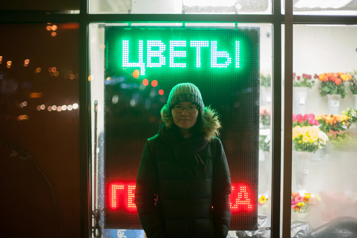 Woman in a black parka standing near neon signage at night