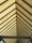 A symmetrical view of a roof structure with a series of evenly spaced triangular beams converging to form a perspective. The roof panels are a translucent material that allows light to filter through, creating a warm glow.