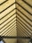A symmetrical view of a roof structure with a series of evenly spaced triangular beams converging to form a perspective. The roof panels are a translucent material that allows light to filter through, creating a warm glow.