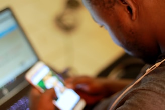 A person using a laptop with a cell phone beside it, focused on the screen.