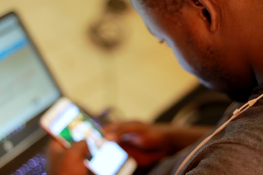 A person using a laptop with a cell phone beside it, focused on the screen.