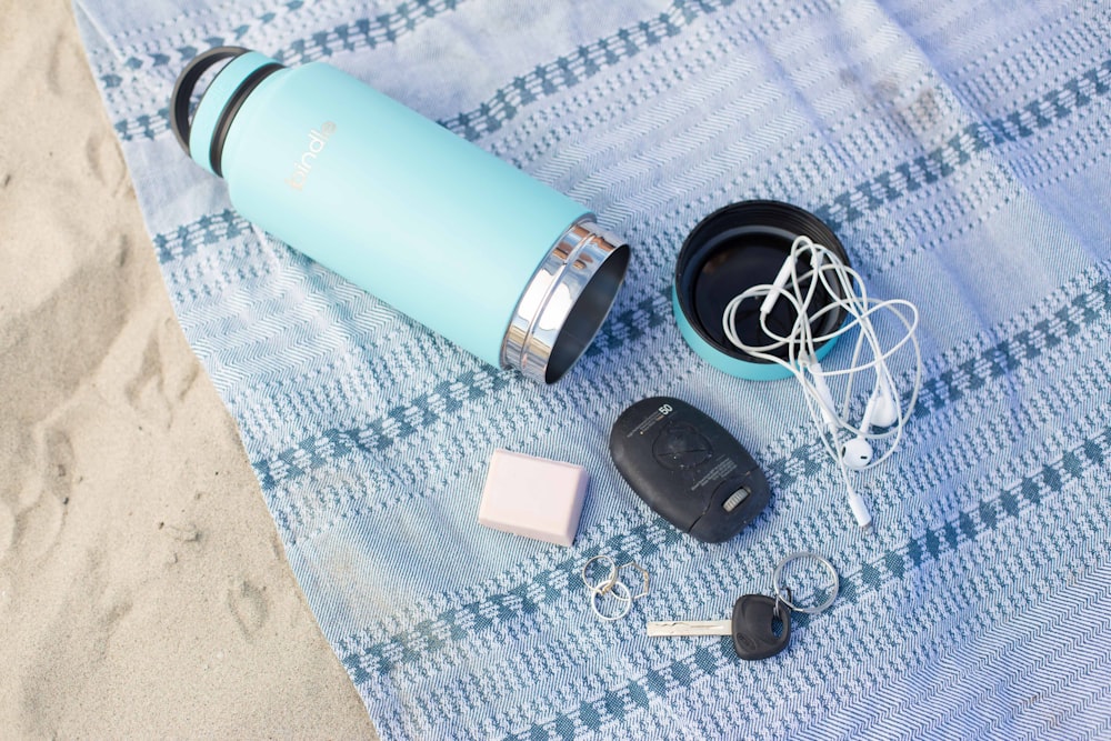 Tasse de voyage en acier inoxydable turquoise avec porte-clés, clé et écouteurs sur textile bleu