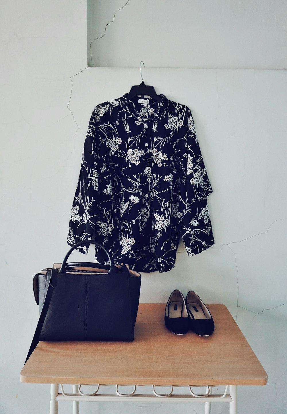black and white floral sport shirt hanging beside black leather 2-way tote bag and ballet flats