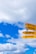 A vibrant yellow signpost against a background of a bright blue sky with scattered white clouds. The signpost has arrows pointing to various locations such as the Equator, Vancouver, Los Angeles, and the Tropic of Capricorn, with distances marked in nautical miles and kilometers.