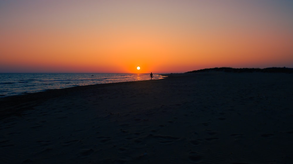 uma pessoa em pé em uma praia ao pôr do sol