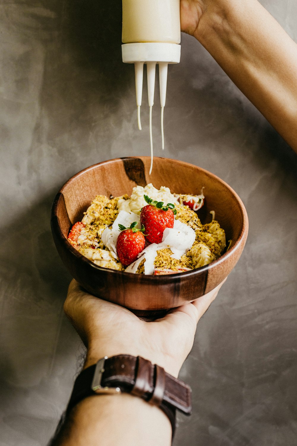 person putting cream on bowl with strawberries