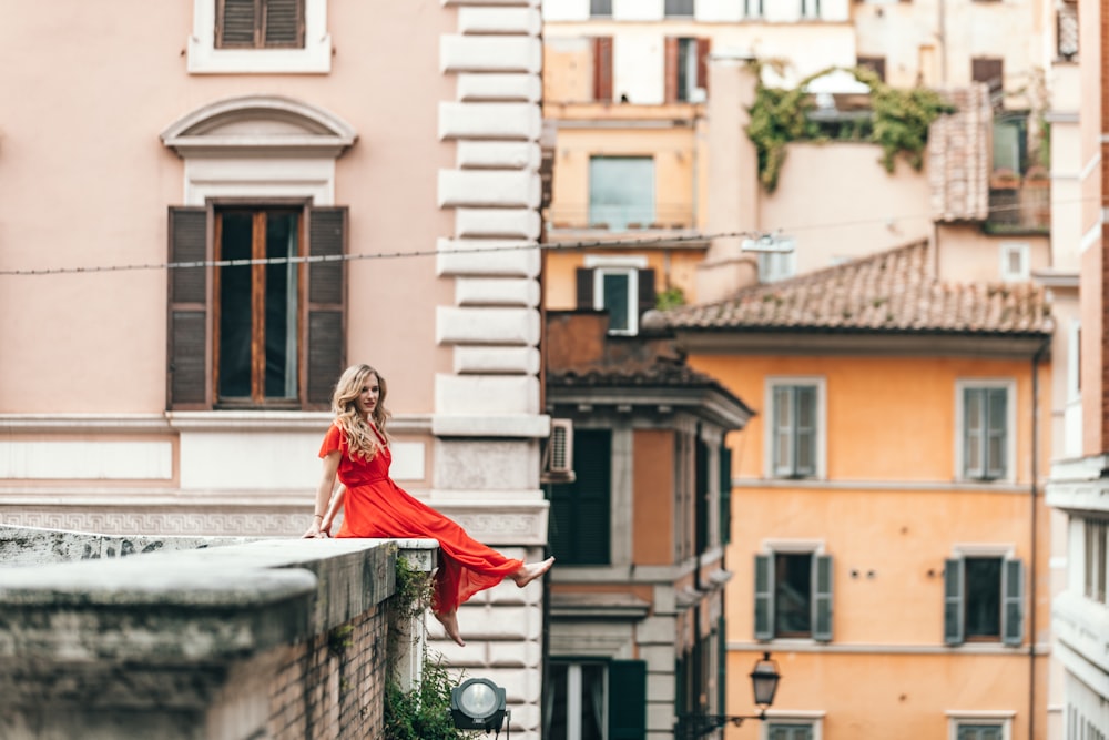 woman wearing red dress sitting on the edge of building roof