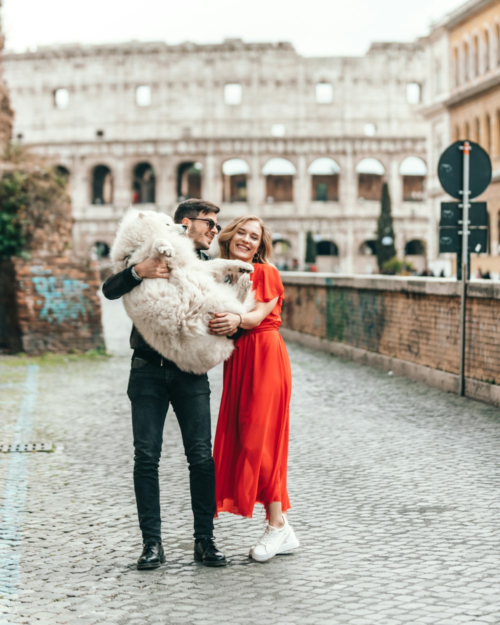 smiling and standing man and woman carrying white dog