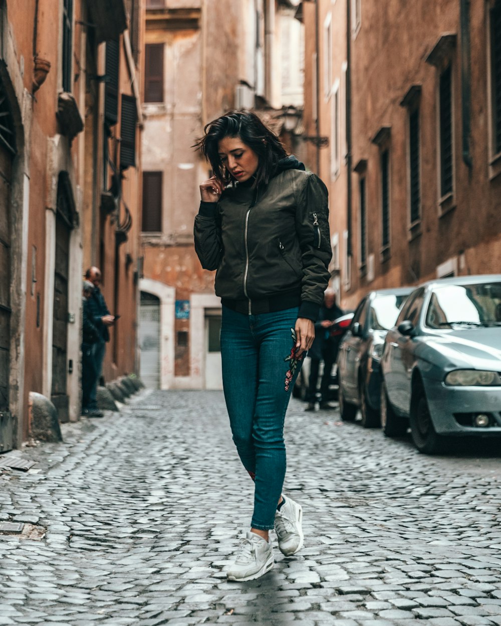 woman wearing black bomber jacket standing on alley during daytime