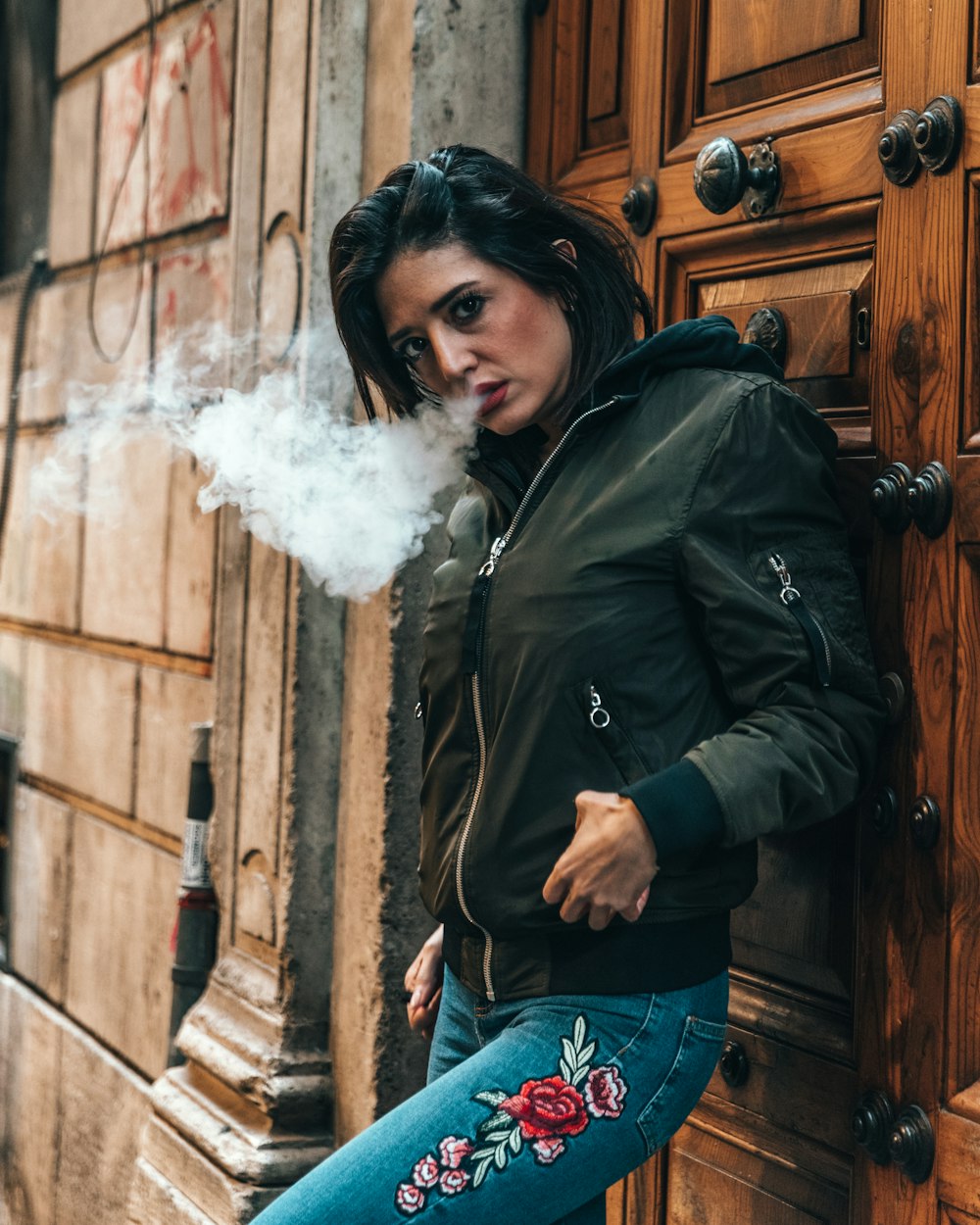 woman blowing smoke while leaning on brown wooden door