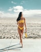 standing woman wearing yellow bikini holding yellow bottle