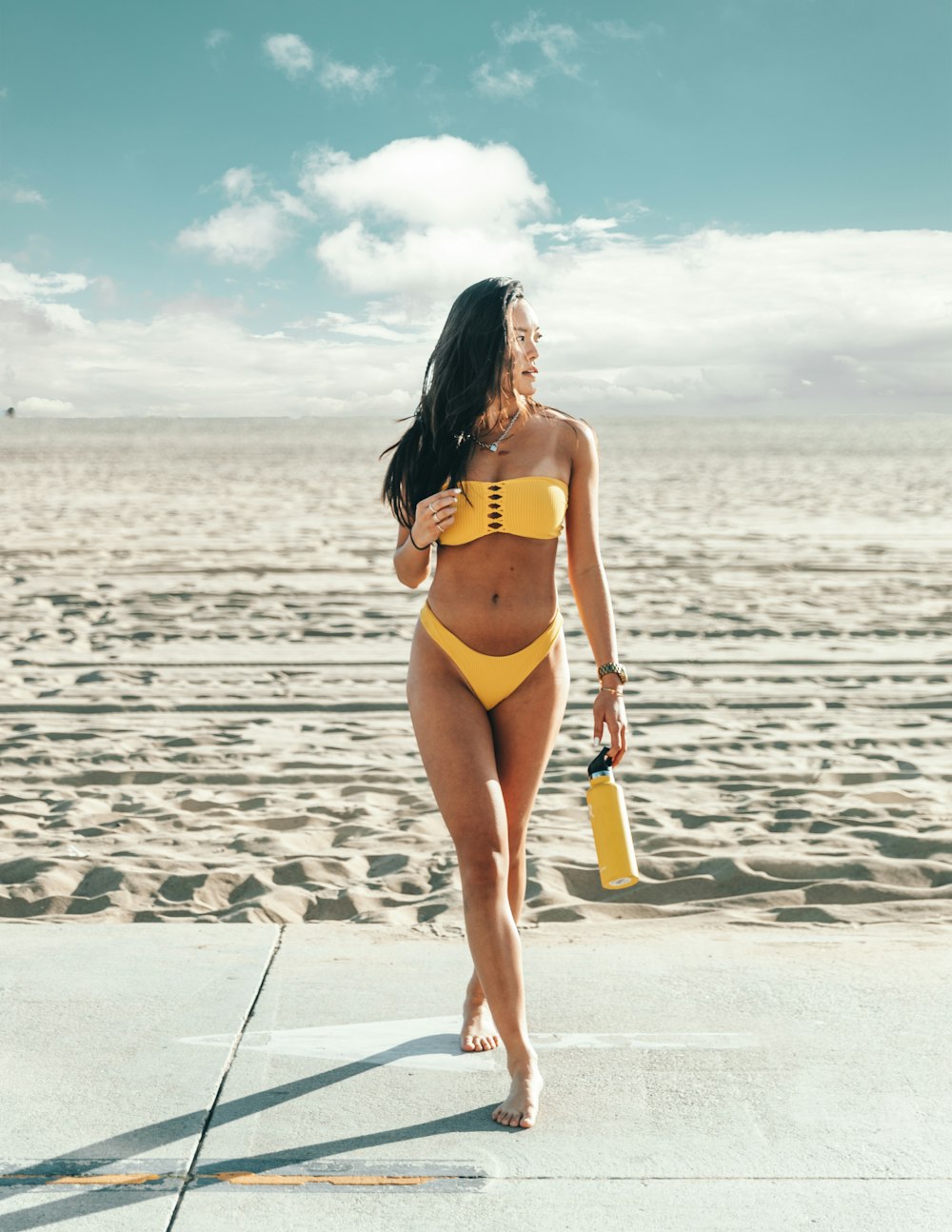 Stehende Frau im gelben Bikini mit gelber Flasche