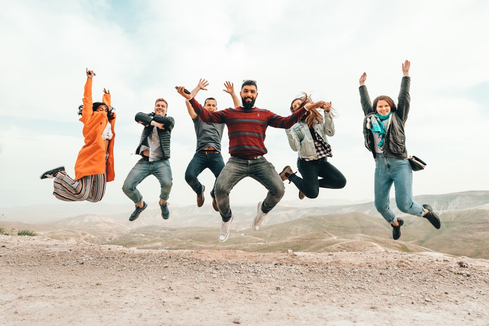 six group of people jumping on hill