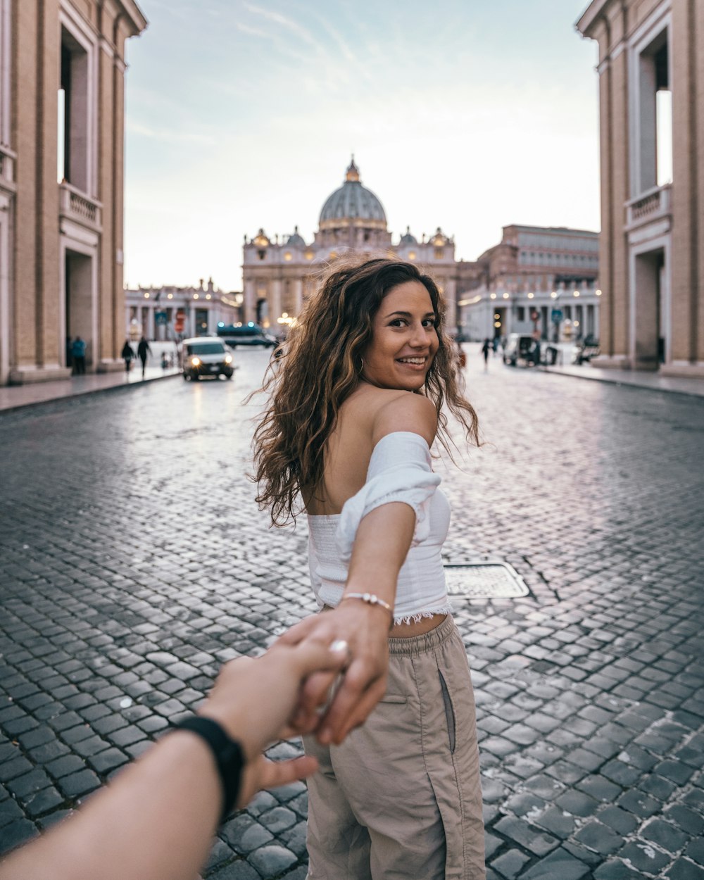 Mujer con top blanco y pantalones marrones arrastrando la mano de la persona