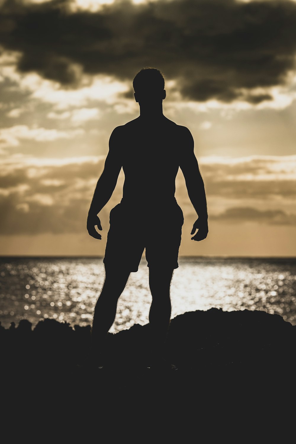silhouette photography of man standing on rock formation near body of water
