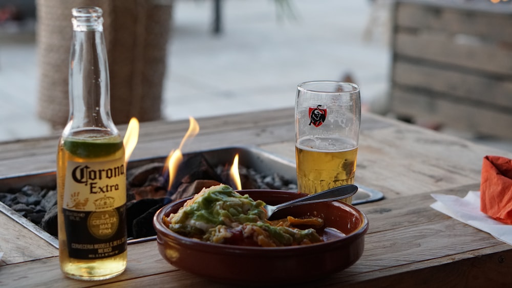 a wooden table topped with a bowl of food and a bottle of beer