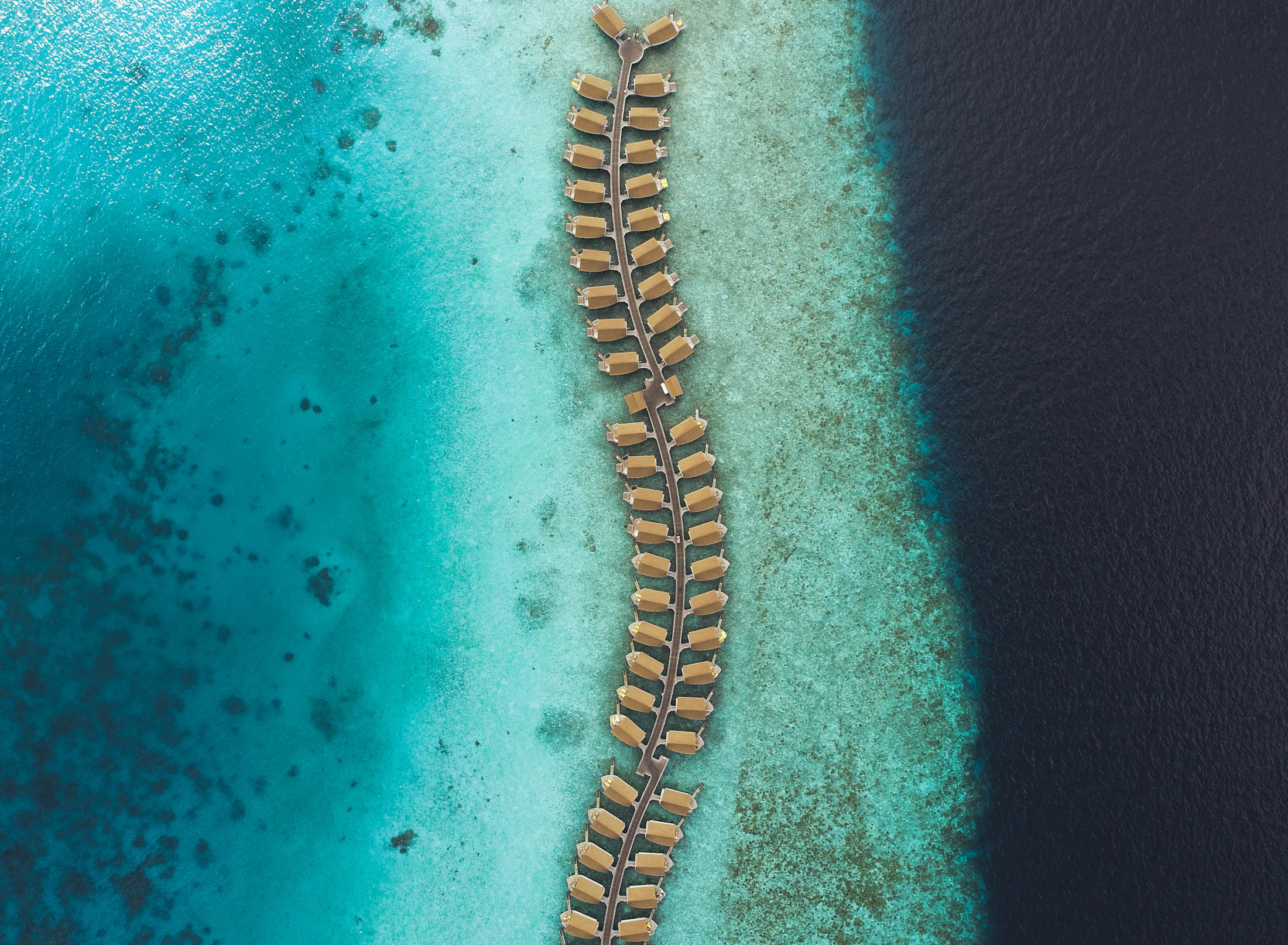 Water villas extending across a turquoise Maldivian reef and deep blue ocean