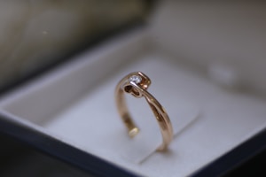 A gold ring with a single diamond set on top, presented in an elegant jewelry box with a soft, neutral background.