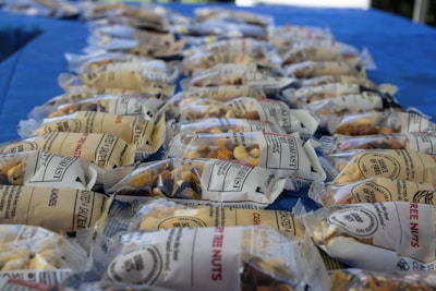 Numerous sealed packets of assorted nuts are neatly arranged on a blue tablecloth. The packaging is transparent, allowing a clear view of the nut mix inside.